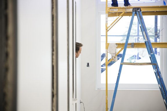 A man peeks his head into a studio where a ladder has been set up for construction.